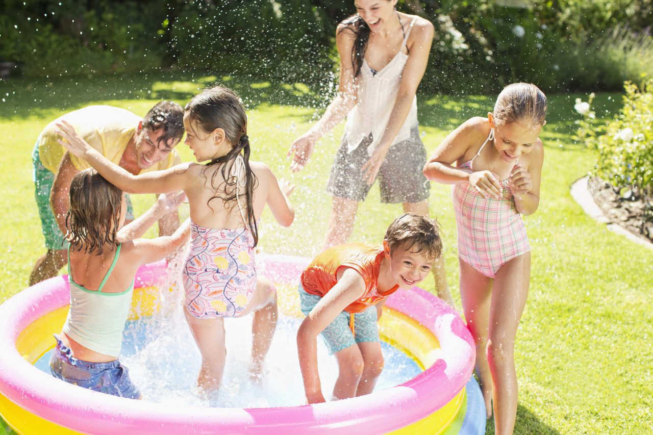 Blended family playing in paddling pool in sunny garden